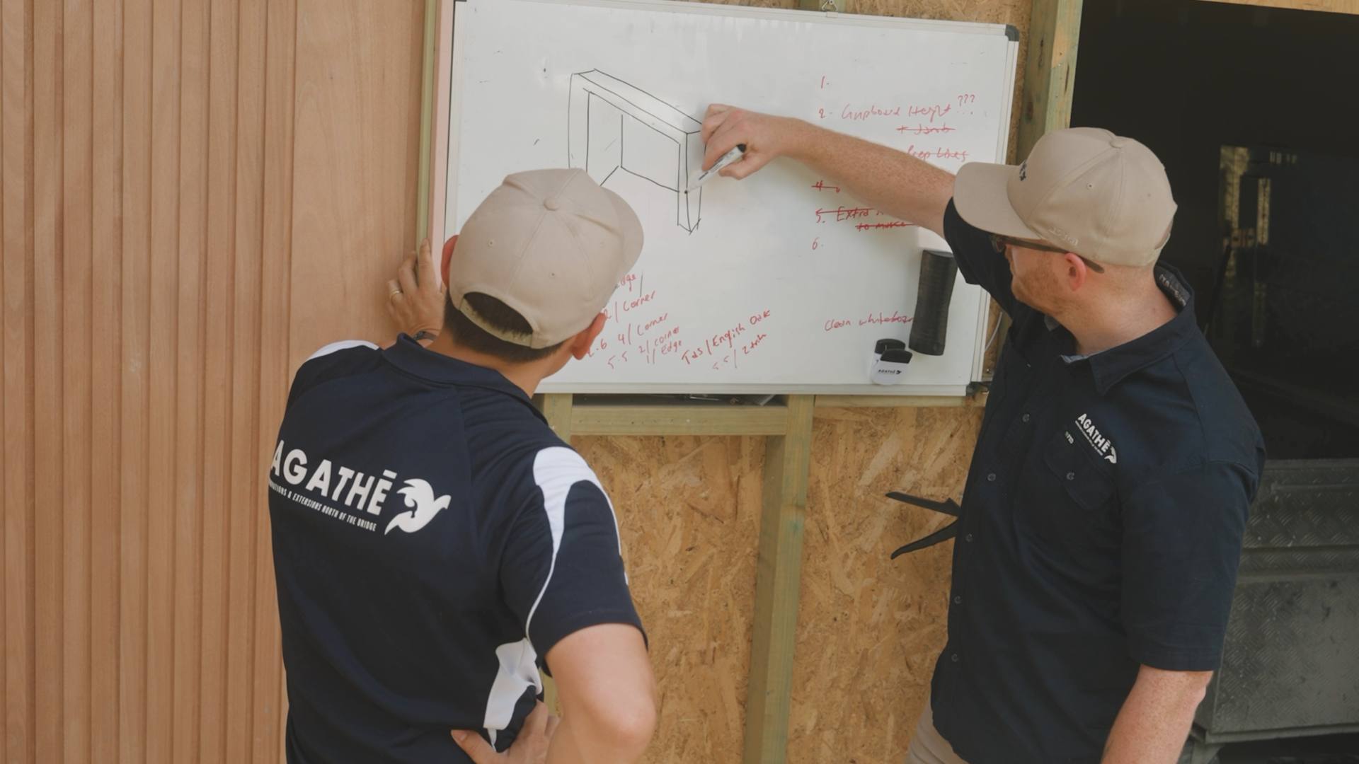 Two AGATHĒ Builders team members planning a project at a whiteboard on site