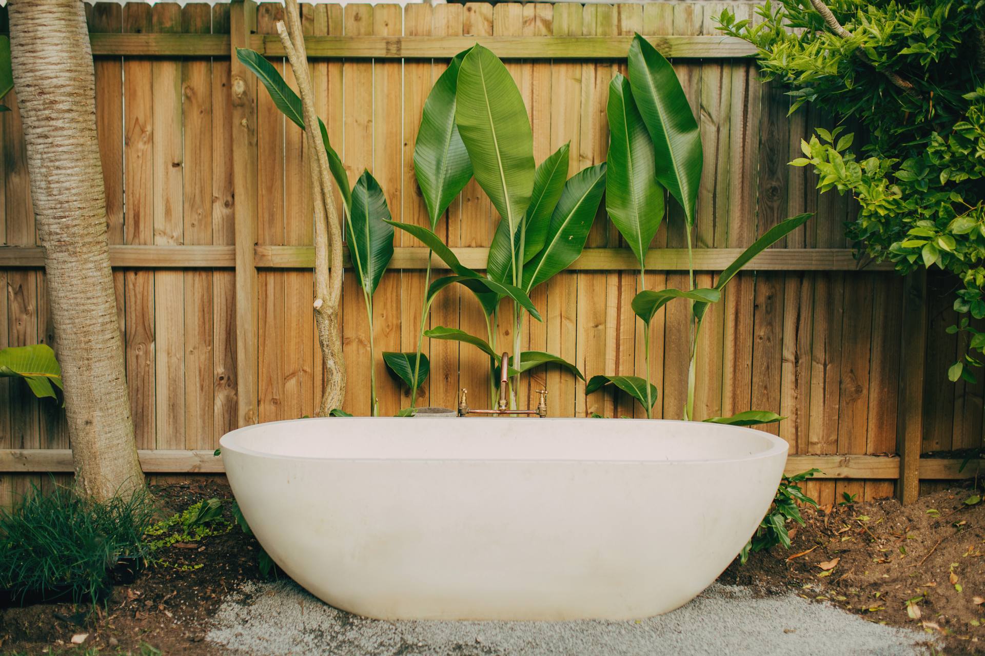 Freestanding outdoor bath in a private courtyard with a timber screen and tropical planting