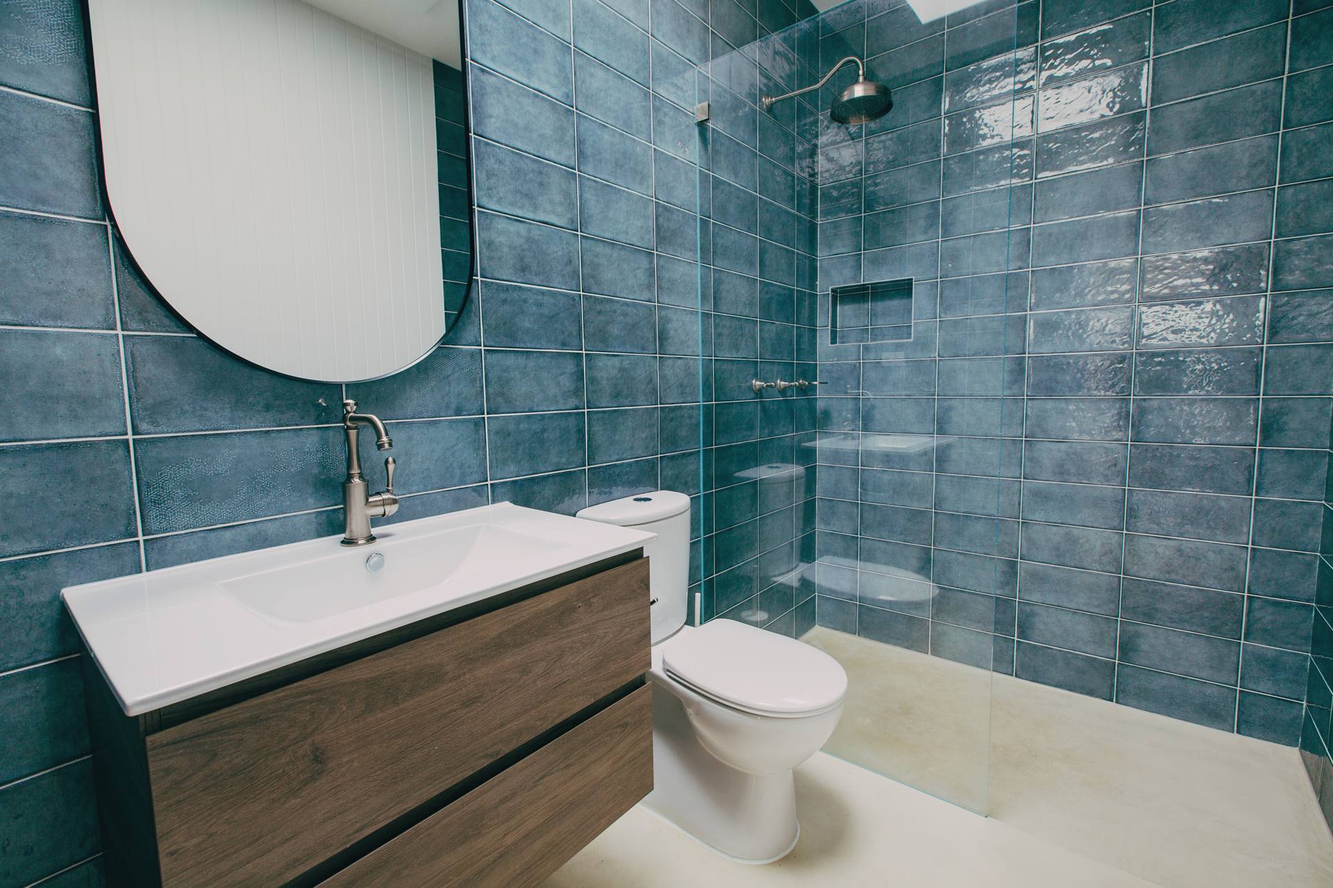 Bathroom with deep teal tiling, a round mirror, timber vanity and micro-cement basin in the Pymble home