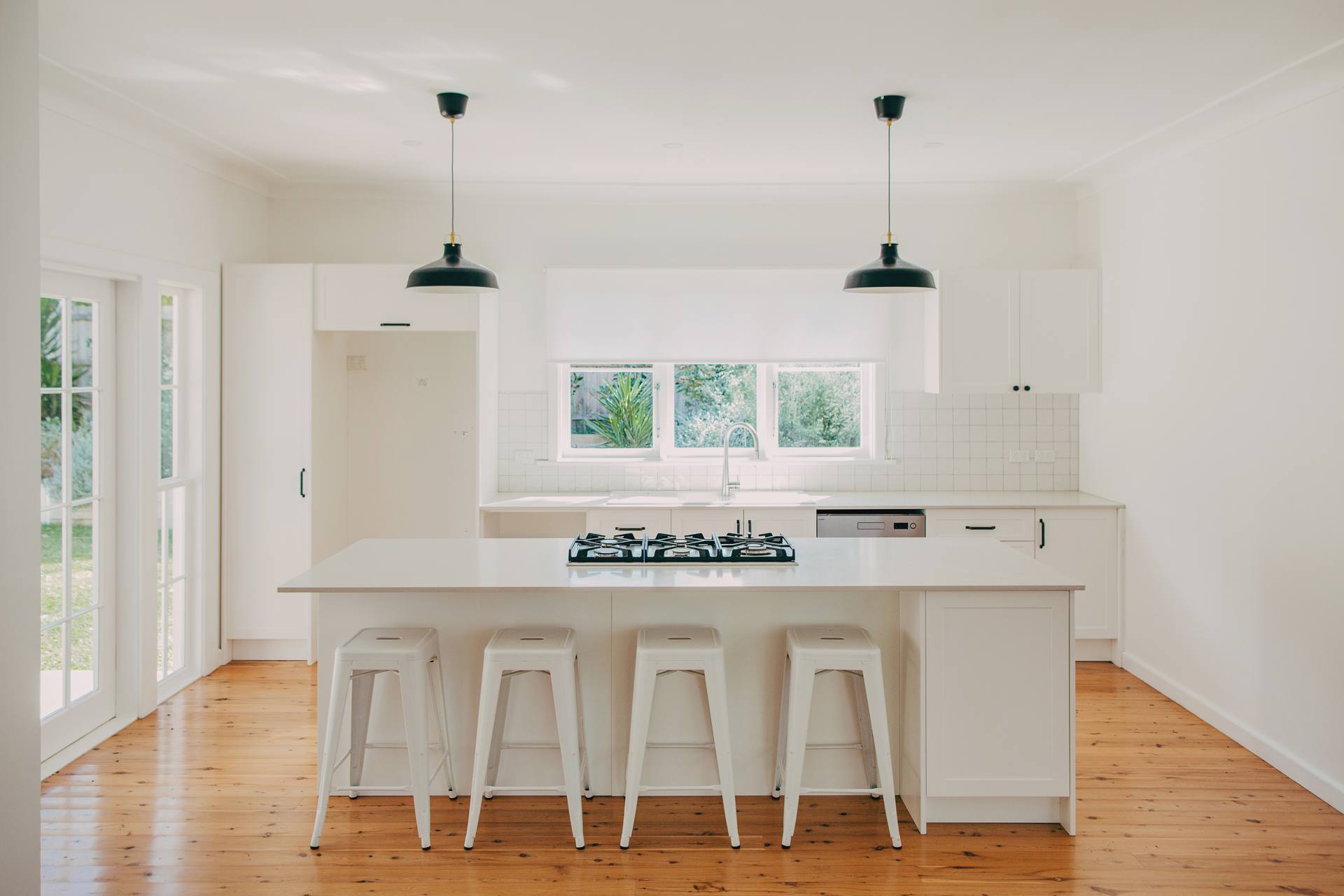 New kitchen with a white island bench, pendant lighting and timber flooring in the renovated Pymble home